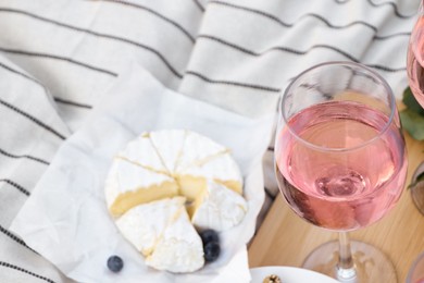 Glass of delicious rose wine and food on white picnic blanket, closeup