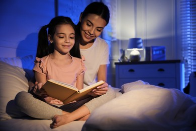 Mother with little daughter reading fairy tale in dark bedroom