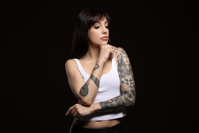 Beautiful woman with tattoos on arms against black background