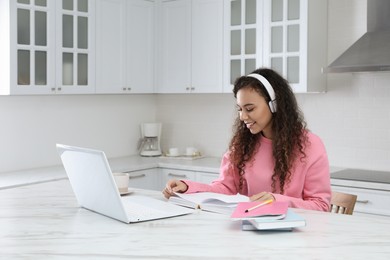 African American woman with modern laptop and headphones studying in kitchen. Distance learning