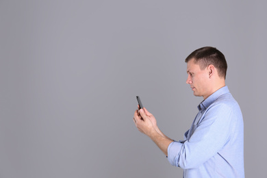 Man unlocking smartphone with facial scanner on grey background, space for text. Biometric verification