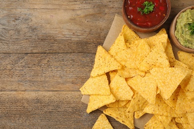 Mexican nacho chips with different sauces on wooden background, flat lay. Space for text