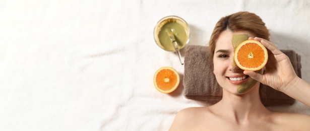 Woman with mask on face and cut orange relaxing in spa salon, top view with space for text. Banner design
