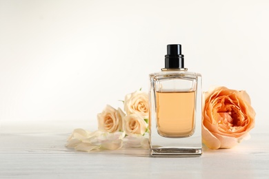 Photo of Elegant bottle of perfume and flowers on light background, space for text