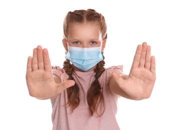 Little girl in protective mask showing stop gesture on white background. Prevent spreading of coronavirus