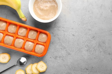 Banana puree in ice cube tray with fresh banana fruits on grey table, flat lay. Space for text