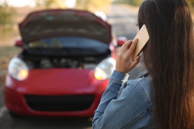Photo of Young woman talking on phone near broken car outdoors, closeup