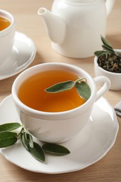 Cup of aromatic sage tea with fresh leaves on wooden table