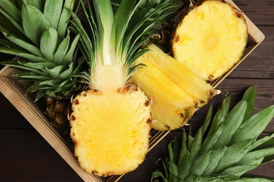 Photo of Tasty cut pineapples in crate on wooden table, flat lay