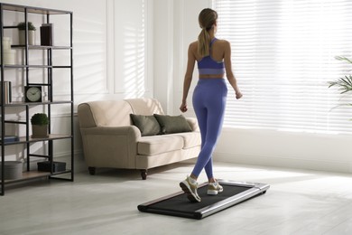 Sporty woman training on walking treadmill at home, back view