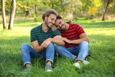 Portrait of happy gay couple sitting on grass in park
