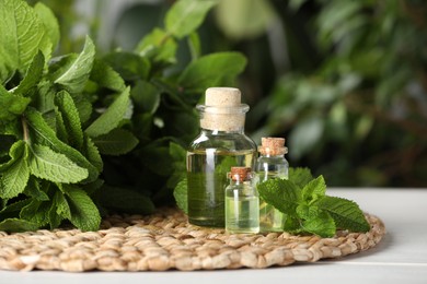 Bottles of mint essential oil and green leaves on white wooden table