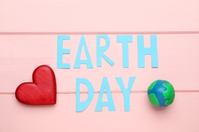 Words Earth Day, plasticine planet and decorative heart on pink wooden table, flat lay