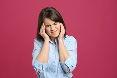 Young woman suffering from migraine on crimson background