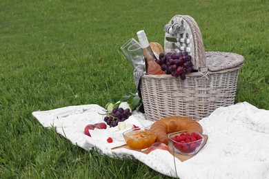 Photo of Picnic blanket with tasty food, flowers, basket and cider on green grass outdoors. Space for text