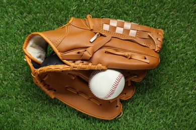 Photo of Catcher's mitt and baseball ball on green grass, top view. Sports game