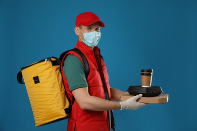 Courier in protective mask and gloves holding order on blue background. Food delivery service during coronavirus quarantine