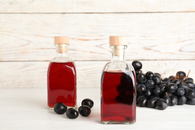 Glass bottles with wine vinegar and fresh grapes on wooden table