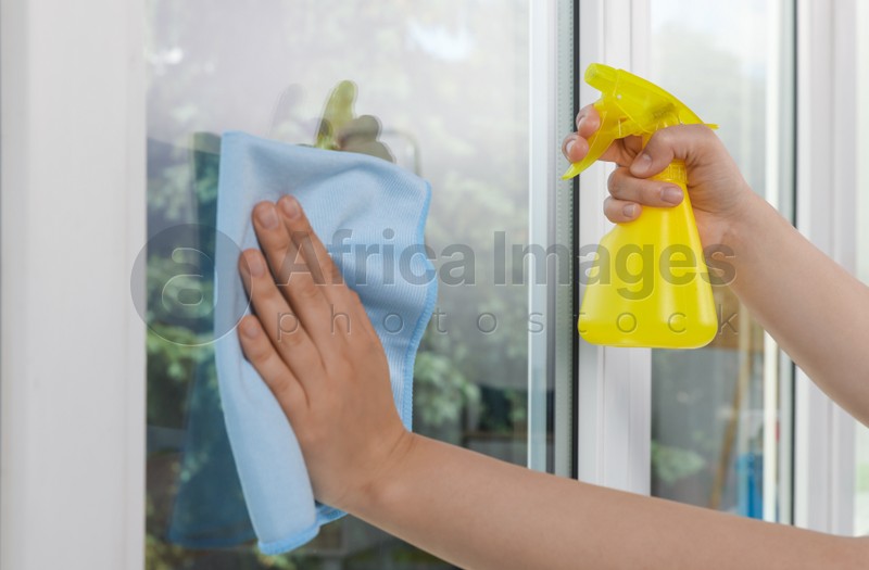 Photo of Woman cleaning window glass with rag and spray indoors, closeup
