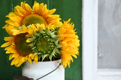 Bouquet of beautiful sunflowers in tin near window outdoors