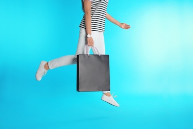 Woman jumping with paper shopping bag on color background. Mock up for design