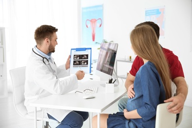 Gynecology consultation. Doctor showing ultrasound of baby to future parents in clinic