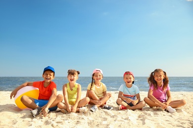Photo of Group of happy children sitting on sand at sea beach. Summer camp