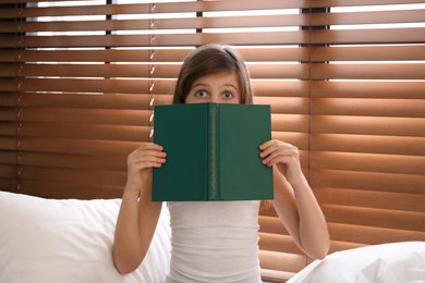Photo of Emotional preteen girl with book on bed near window