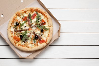 Photo of Tasty pizza with anchovies, arugula and olives on white wooden table, top view. Space for text