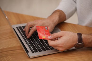 Photo of Man using laptop and credit card for online payment at wooden desk, closeup
