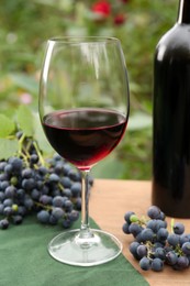 Red wine and grapes on wooden table outdoors, closeup