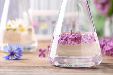 Flask with lilac flowers on wooden table, closeup. Essential oil extraction