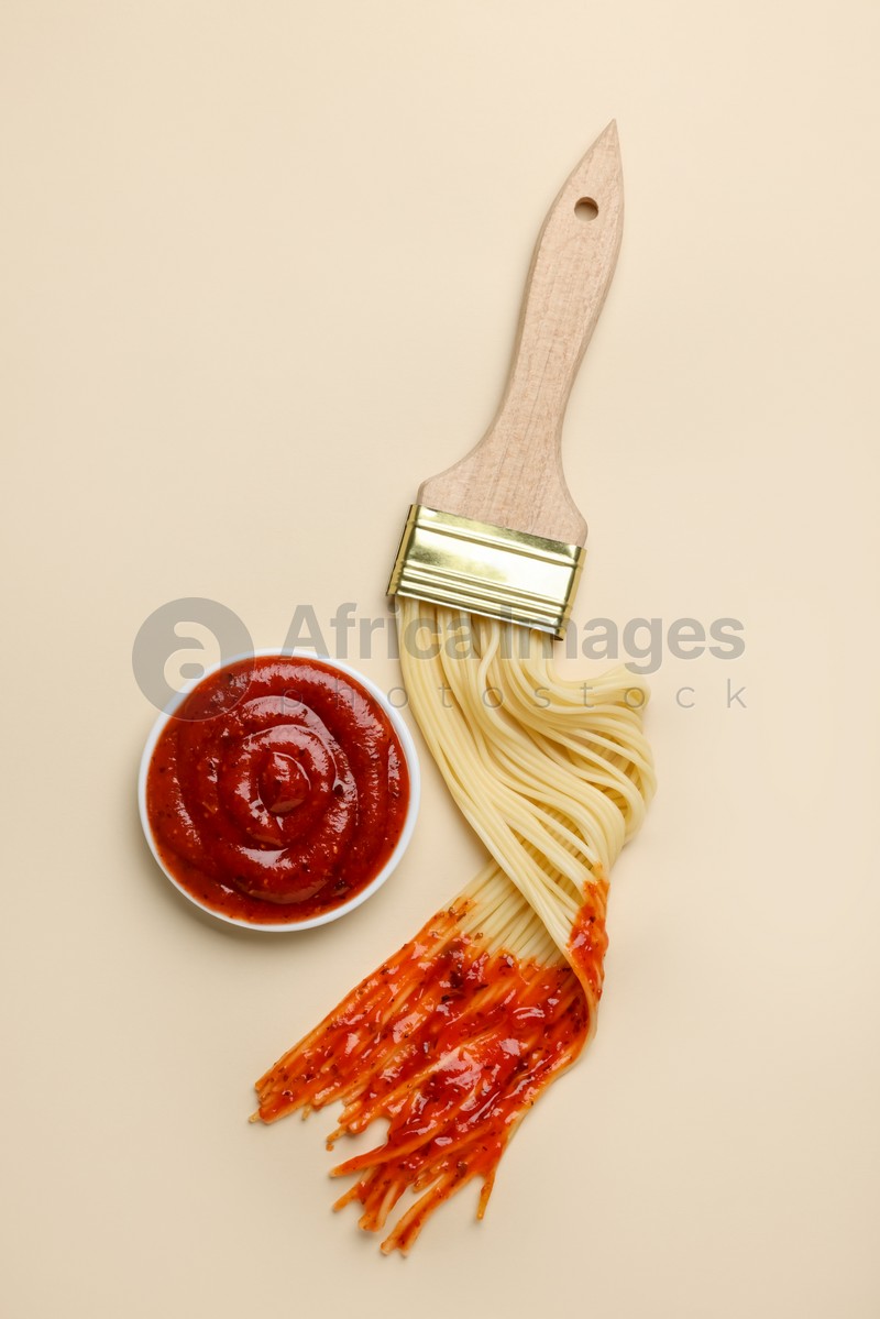 Brush painting with spaghetti dipped in ketchup on beige background, flat lay. Creative concept