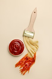 Photo of Brush painting with spaghetti dipped in ketchup on beige background, flat lay. Creative concept