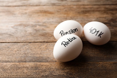 Eggs with words PENSION, RETIRE and 401k on wooden background. Space for text