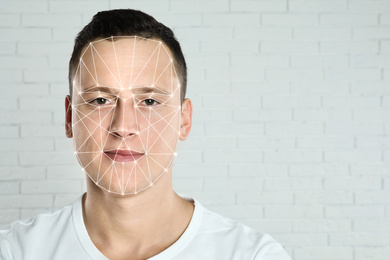 Facial recognition system. Young man with biometric identification scanning grid near brick wall, space for text