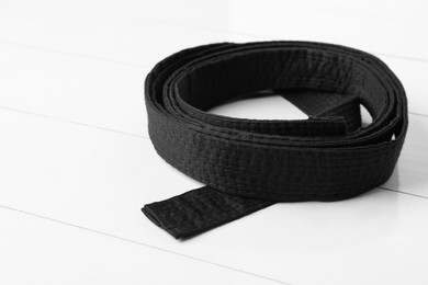 Rolled black belt on white wooden background, closeup. Oriental martial arts