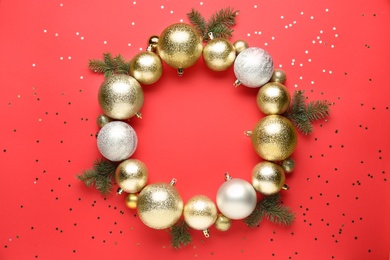 Beautiful festive wreath made of color Christmas balls and fir tree branches on red background, top view