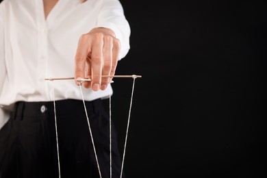 Woman in formal outfit pulling strings of puppet on black background, closeup. Space for text