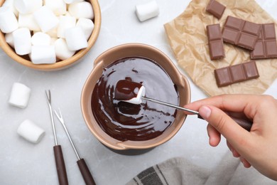 Photo of Woman dipping marshmallow into melted chocolate at light grey marble table, above view