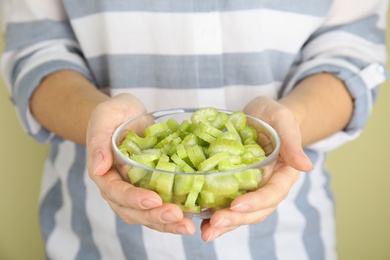 Photo of Woman holding bowl with cut celery on light background, closeup