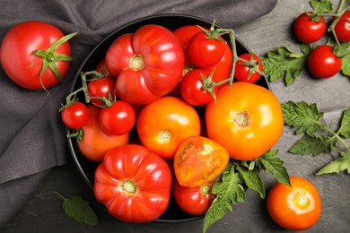 Many different ripe tomatoes with leaves on black table, flat lay