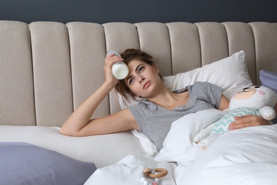 Exhausted young mother with toy and bottle of milk in bed at home