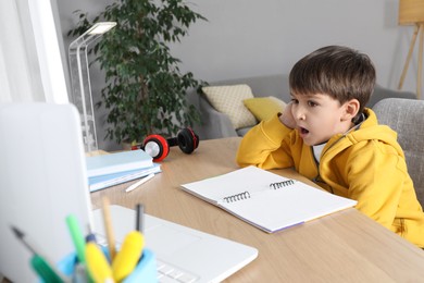 Photo of Cute little boy with modern laptop studying online at home. E-learning