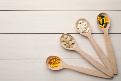 Spoons with different dietary supplements on white wooden table, flat lay. Space for text