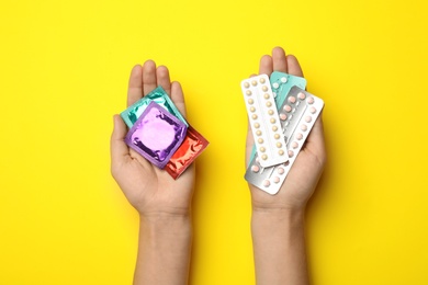 Woman holding condoms and birth control pills on yellow background, top view. Safe sex