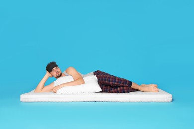 Man wearing sleeping mask on soft mattress against light blue background