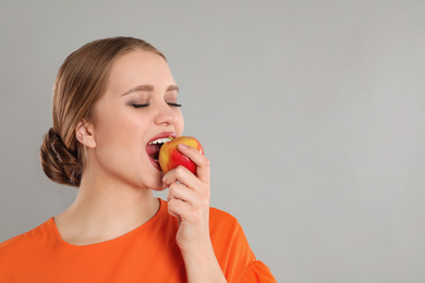 Photo of Young woman with apple on grey background, space for text. Vitamin rich food