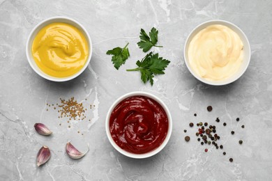 Photo of Bowls with mustard, ketchup and mayonnaise on light grey table, flat lay