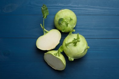 Whole and cut kohlrabi plants on blue wooden table, flat lay